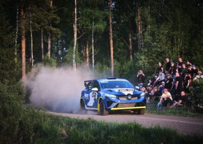 The driver of a Renault rally car expertly handles the steering wheel through a challenging section of the course.