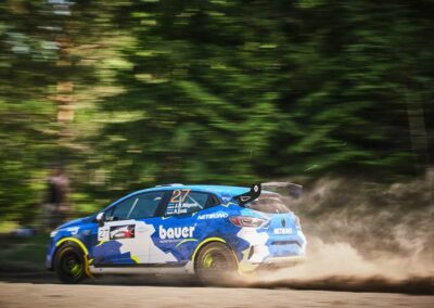 Renault rally car kicking up dust on a gravel track during an intense race.