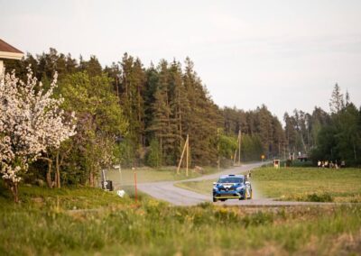 A Renault rally car speeds past spectators, leaving a cloud of dust in its wake.