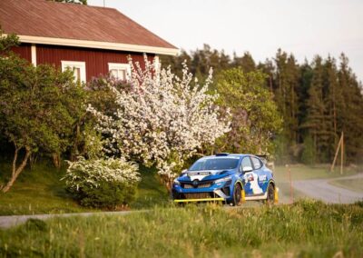 The driver of a Renault rally car expertly handles the steering wheel through a challenging section of the course.