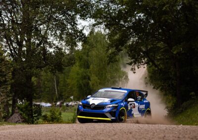 Renault rally car kicking up dust on a gravel track during an intense race.