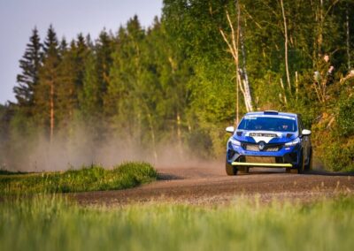 Sunlight glinting off the vibrant livery of a Renault rally car as it navigates a tight corner.