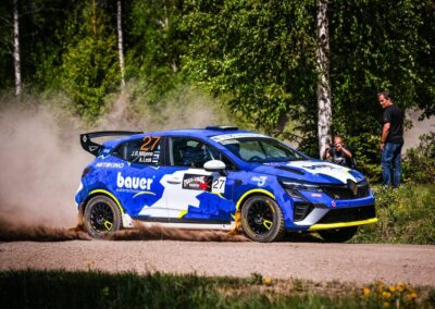 Renault rally car kicking up dust on a gravel track during an intense race.