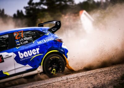 Renault rally car kicking up dust on a gravel track during an intense race.