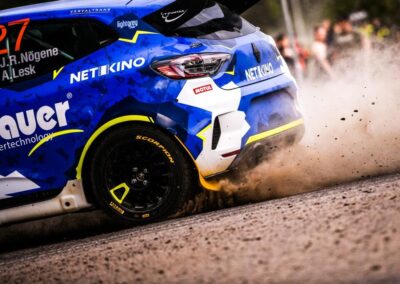 Renault rally car kicking up dust on a gravel track during an intense race.